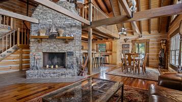A spacious living area with a stone fireplace, wooden beams, and a glass coffee table.
