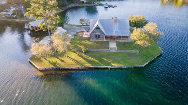 Una cabaña junto al lago con un muelle, rodeada de árboles y una vista despejada del lago.