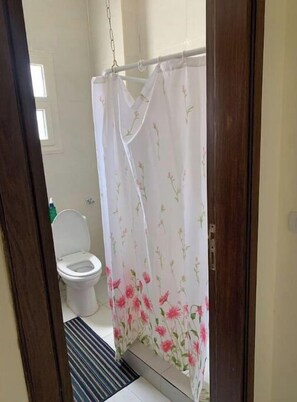 Enter a bathroom with a shower area and toilet, featuring a floral curtain and a window above.