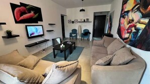 A modern living room with a beige sofa, a coffee table, and a TV. There are two chairs and a painting on the wall. - Alrehab city luxury apartment (Cairo Governorate)