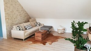 Une chambre de style loft moderne avec un plafond en pente, un canapé beige, une commode en bois, un tapis en cuir et une plante en pot.