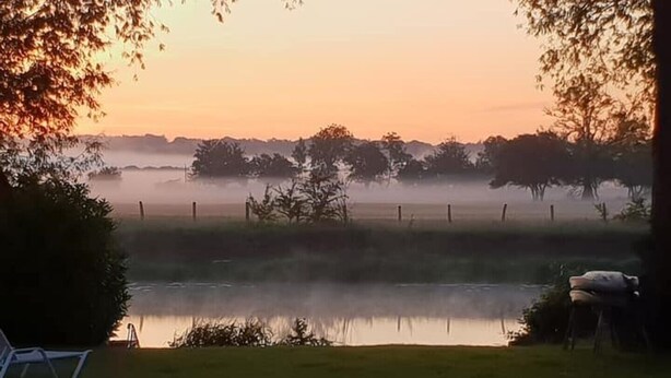 Un paysage extérieur paisible, avec une étendue d’eau, des arbres et une zone herbeuse.