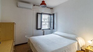 Ein Schlafzimmer mit einem Bett, einem Holzschrank, einem Fenster mit Metallgitter und einer roten Pendelleuchte.