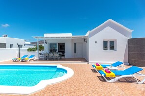 En modern, vit villa med pool, utomhusmöbler och en uteplats.