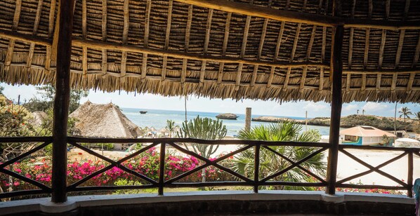 A thatched-roof gazebo with a view of the sea and beach.