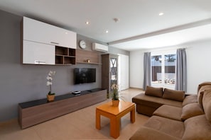 Een moderne woonkamer met een flatscreen televisie, een houten kast, een bank en een kleine tafel met een plant.