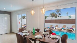 A dining area with a pool view, including a table set for four, a bottle of water, and a bottle of wine.