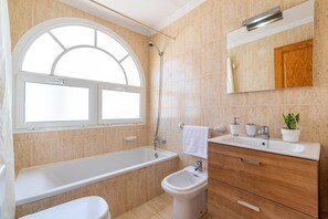 A bathroom with a bathtub, a bidet, a sink, a mirror, and a window.