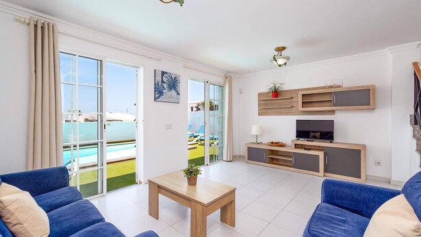 Ein modernes Wohnzimmer mit Blick auf einen Pool, mit blauen Sofas, einem Holztisch und einem integrierten Fernseher.