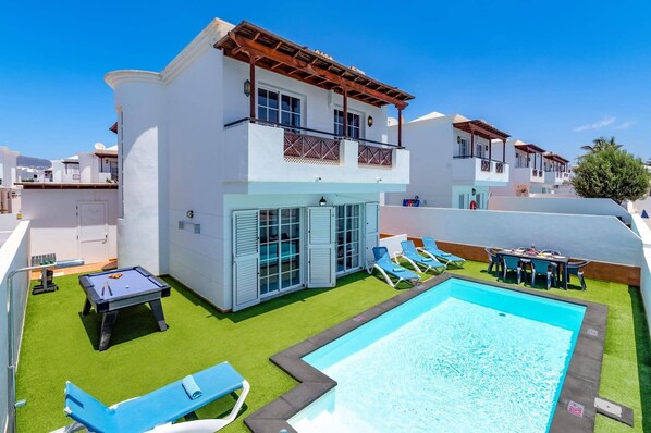 A two-story building with a swimming pool, outdoor seating, and a covered patio area.