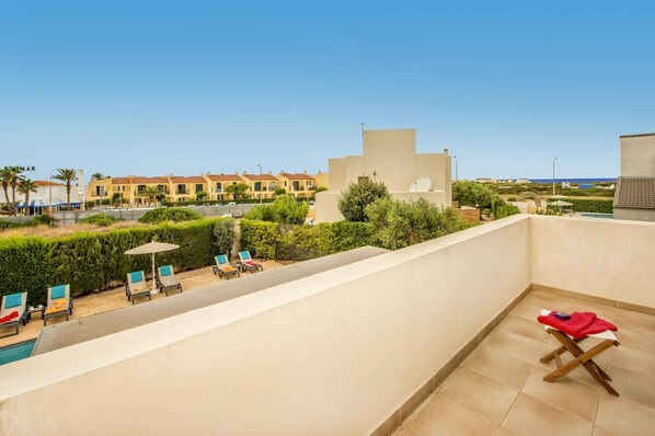 A rooftop terrace with a pool, lounge chairs, and a view of the sea and buildings.