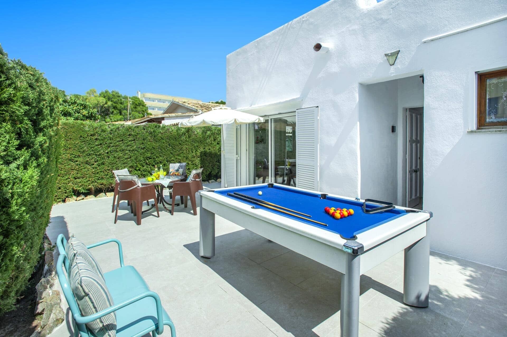 A pool table in an outdoor patio area with a white building in the background.