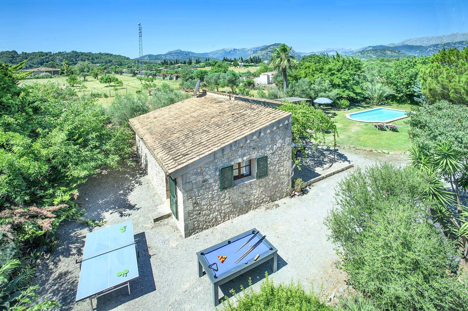 A stone building with a tiled roof, a pool, and outdoor tables and chairs.