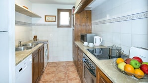 Una cocina compacta con lavavajillas, fregadero, microondas, estufa y un frutero sobre la encimera.