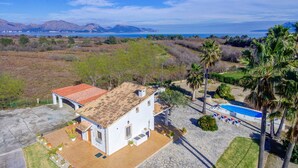 A white building with a tiled roof, a swimming pool, and palm trees. - Villa Can Idu by Villa Plus (Mallorca)