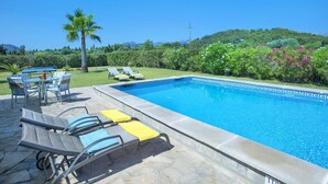 A swimming pool with lounge chairs and a table, surrounded by greenery and a clear sky. - Villa Can Rasca by Villa Plus (Mallorca)