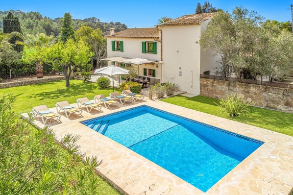 A swimming pool with lounge chairs, a patio with an umbrella, and a building with a tiled roof.