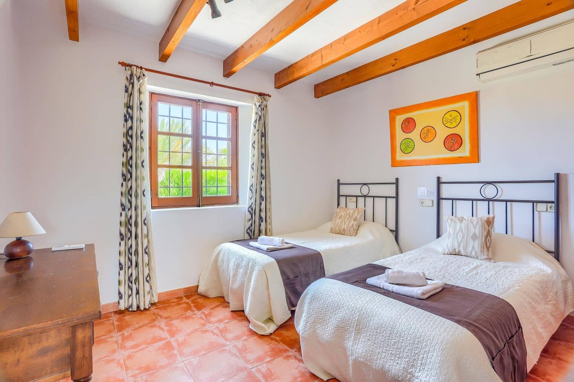 Quarto com duas camas, uma janela com cortinas, um quadro na parede e teto de madeira.