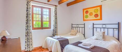 Quarto com duas camas, uma janela com cortinas, um quadro na parede e teto de madeira.
