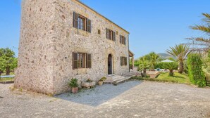 A two-story stone building with a gravel driveway and a small garden with palm trees. - Villa Can Xanet de Baix by Villa Plus (Mallorca)