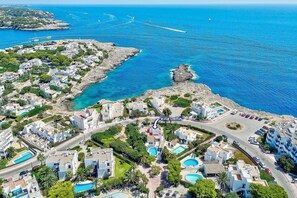 An aerial view of a coastal residential area with villas, clear blue waters, and rocky terrain.