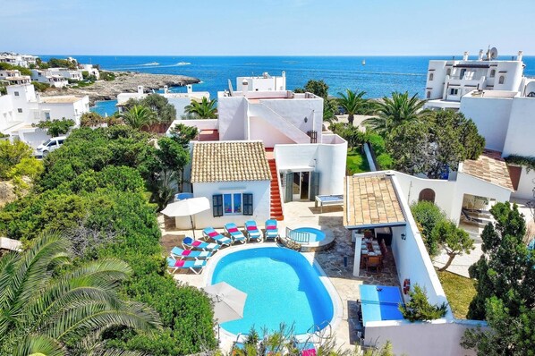 A resort with a swimming pool, lounge chairs, and a view of the sea.