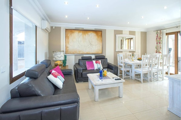 A spacious living room with a sofa, a coffee table, and a dining area with white chairs and a table.