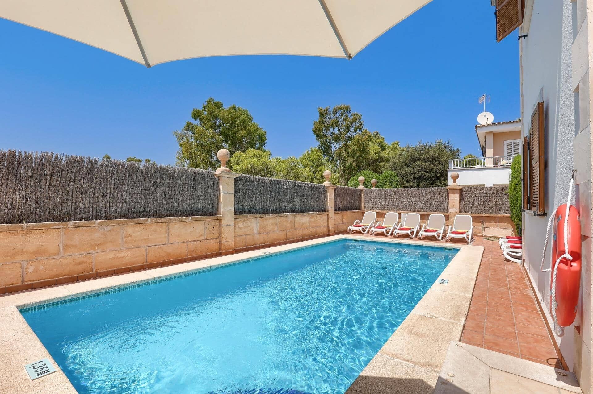 A swimming pool with lounge chairs, a lifebuoy, and a clear blue sky.