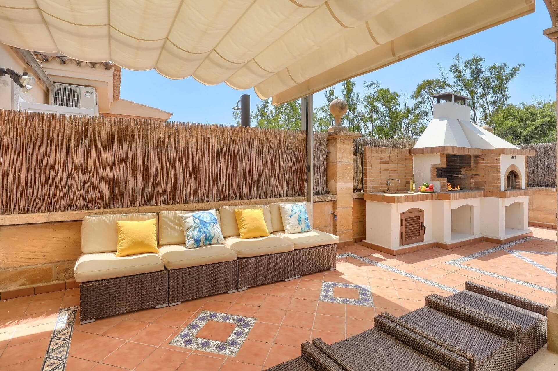 An outdoor patio with a wicker sofa, a barbecue area, and a tiled floor.