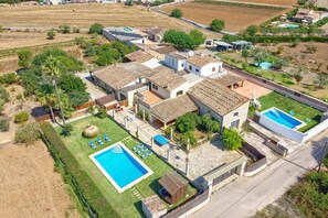 Un quartier résidentiel doté de deux piscines, d’une grande maison avec un toit en tuiles et entouré de champs.