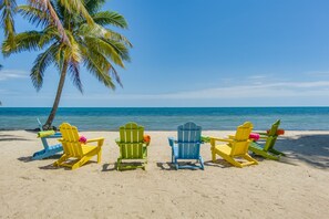 Eine Reihe bunter Adirondack-Sessel am sandigen Strand mit einer Palme und Blick aufs Meer.