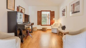 Ein Wohnzimmer mit einem Klavier, einem weißen Sessel, einer Couch und Holzboden.