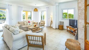 Un salon spacieux comprenant un canapé, des fauteuils, une table basse, un téléviseur et une vue sur la verdure environnante.