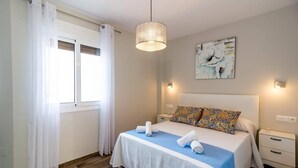 Ein Schlafzimmer mit einem Bett, einem Nachttisch, einer Lampe, einem Fenster mit Vorhängen und einem Bild an der Wand.