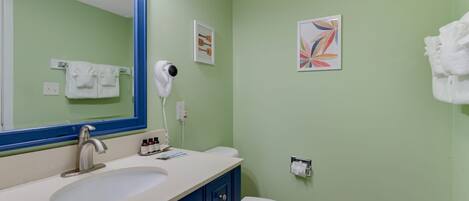 A bathroom with a large mirror, a sink, a toilet, and a hairdryer on the wall.