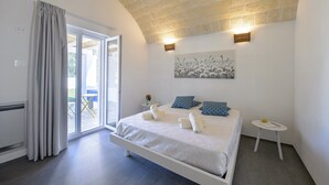 Une chambre à coucher avec un lit, une petite table de chevet, une lampe fixée au mur et une vue sur l’extérieur, visible à travers une porte vitrée.