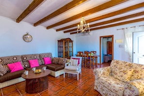 A living room with a sofa, armchair, dining table, and chairs. - Villa Encinas by Villa Plus (Valtocado)