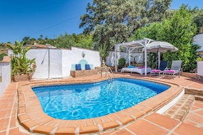 A swimming pool with a brick border, a white wall with a lion emblem, and a covered seating area with lounge chairs. - Villa Encinas by Villa Plus (Valtocado)