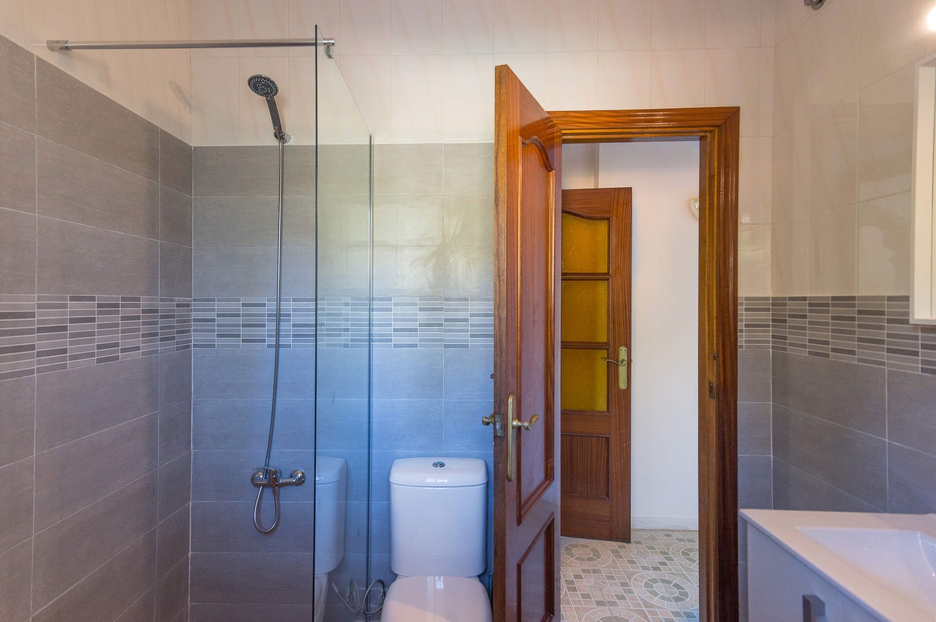 A bathroom with a glass shower enclosure, a toilet, and a wooden door.