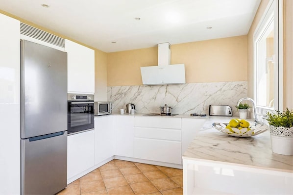 A modern kitchen with white cabinetry, a stainless steel refrigerator, a built-in oven, a microwave, a gas stove, and a sink.