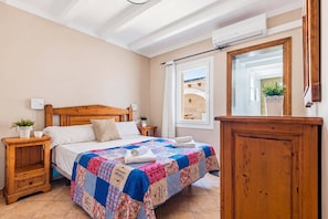 Ein Schlafzimmer mit einem Holzbett, einer Steppdecke, einem Nachttisch mit Pflanze, einem Fenster mit Aussicht und einem Spiegel.