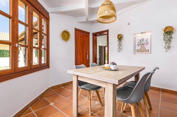 Een eetgedeelte met een houten tafel, zwarte stoelen, een hanglamp en een lijst met een afbeelding aan de muur.