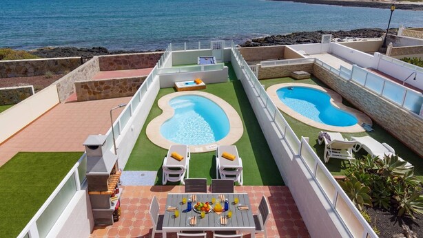A rooftop pool area with two pools, a dining table with chairs, and a view of the sea. - Villa Atlantico by Villa Plus (Corralejo)