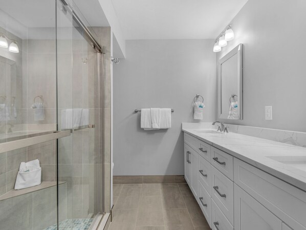 Un bany modern amb una cabina de bany de vidre, un mirall gran i un moble de bany amb rentapelats i calaixos.