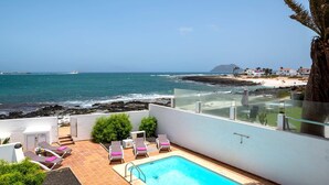 A rooftop pool with lounge chairs, a clear view of the ocean, and a rocky shoreline. - Villa Bella Vista by Villa Plus (Corralejo)