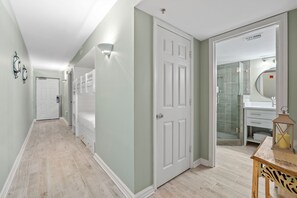A hallway with a light green wall, white doors, and a wooden table with a lantern. - Beach Front, Fully Updated, Destin Harbor, In and Out Pool (Destin)