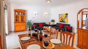 Ein Essbereich mit einem Holztisch, gedeckt für zwei Personen, einer schwarzen Ledersofa mit roten Kissen, einem Holzkabinett mit Glastüren und einem Gemälde an der Wand.