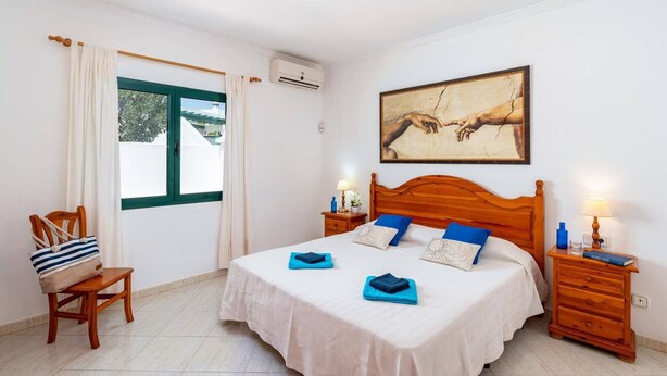 Ein Schlafzimmer mit Bett, Sessel, Nachttisch, Lampe und einem Bild an der Wand.