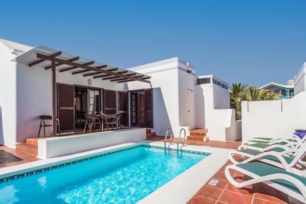 Una piscina con un pérgola y zona de estar al aire libre.