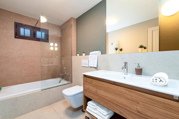 Un baño moderno con ducha envuelta en vidrio, tocador de madera con lavabo blanco y un espejo grande.